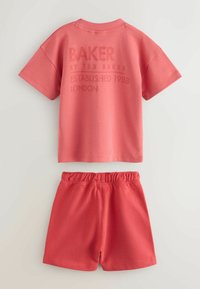 Roze katoenen t-shirt en short set. Het t-shirt heeft reliëf tekst op de achterkant. De shorts hebben een elastische tailleband en een eenvoudig ontwerp.