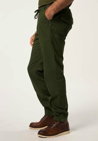 Pantalones cargo verdes con cintura ajustable mediante cordón, bolsillos laterales y puños elásticos, combinados con botas marrones de cordones. Material de algodón duradero.