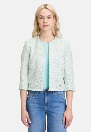 Mintgrüner Tweed-Jacken mit einem kürzeren Design, drei Viertelärmeln und Fransen am Saum. Getragen über einem hellblauen Oberteil mit Jeans.