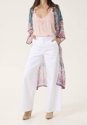 Mujer con camisola rosa con encaje, pantalones blancos de pierna ancha, botas beige con tacón y un kimono largo con estampado floral en tonos azules y rosas.