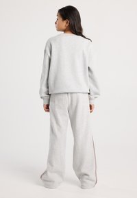 Young woman standing facing away, wearing light gray oversized sweatshirt and matching wide-leg sweatpants with side stripes.