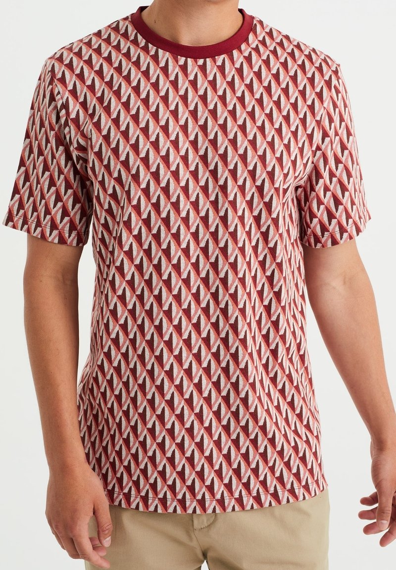 Kortärmad skjorta i röd och beige med ett diamantformat geometriskt mönster; har en rund halsringning med en kontrasterande vinröd kant.