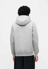 Γκρι φούτερ με κουκούλα από μαλακό υλικό, με ρυθμιζόμενη κουκούλα με κορδόνι, ριμπ μανσέτες και τελείωμα. Η πίσω πλευρά έχει απλό σχέδιο χωρίς γραφικά.