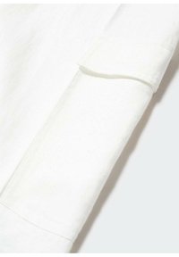 Gros plan d'un poignet de chemise blanche à manches longues avec des coutures visibles et un tissu plié sur un fond clair.