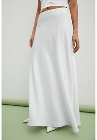 Jupe maxi blanche avec une texture lisse et fluide. Dotée d'une taille haute et associée à des chaussures blanches à bout pointu. Design simple et élégant.