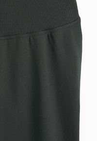 Tamsiai žalia sijonas su dygsniuota elastinga juosmens juosta ir lygaus tekstūros audiniu po siūle.