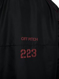 Zwarte stof met rode tekst "OFF PITCH" boven het nummer "223" erop gedrukt.