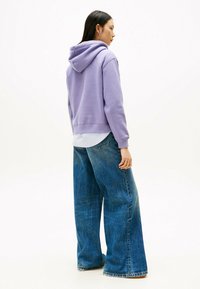 Paarse hoodie met een capuchon, geribbelde manchetten en zoom, gecombineerd met wijde blauwe jeans. De stof lijkt zacht met een gladde textuur.