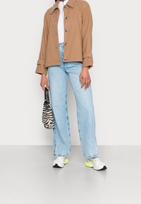 Brun frakk med krave, hvid bluse, lyseblå vide jeans, stribet sort og hvid taske, og multikolore sneakers.