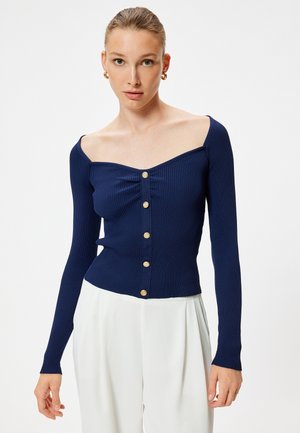 Top largo de manga larga de rayas en color azul marino con escote off-the-shoulder y botones dorados en la parte delantera; silueta ajustada y textura suave.