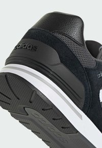 Basket noire avec tige en daim et en maille, dotée d'une semelle en caoutchouc, d'un logo à trois bandes bien visible et d'un capuchon de talon texturé avec une marque.