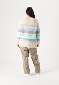 Bežinė megzta kardiganė su horizontaliomis pastelinėms mėlynos, levandų ir rudos spalvomis juostomis. Pasižymi laisvu siluetu ir mėgėjamiems rankogaliams.