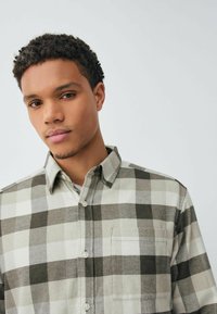 Koszula flanelowa w szaro-białą kratę z kołnierzykiem na guziki, pojedynczą kieszenią na piersi i miękkim, teksturowanym materiałem.