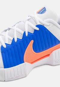 Nike-Sneaker verfügen über ein weißes Mesh-Material mit blauen Gummi-Akzenten und einem orangefarbenen Logo. Das Design umfasst strukturierte Rillen und Schnürsenkel.