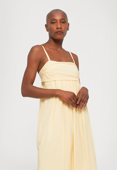 Ljusgul ärmlös klänning med en figurnära bodice, veckad kjol och fyrkantig halsringning. Tillverkad av mjukt tyg med en slät textur.