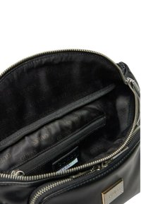 Bolso de mano redondo de imitación cuero negro con interior que incluye un bolsillo con cremallera, forrado con tela estampada que presenta el logo "GUESS", herrajes de cremallera en color plateado.