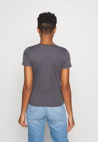 Grå t-shirt med korte ærmer i blødt stof, rund halsudskæring, tætsiddende skjorte og sømløse skuldre, sat sammen med lyseblå jeans.