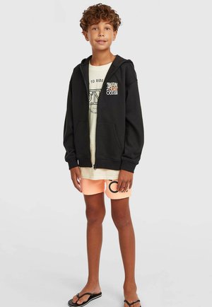 Mustast puuvillasegust lukuga dressipluus, millel esiosas taskud ja värvikas surfiklubi logo. Kantud hele T-särgi ja virsikuvärviliste lühikeste pükstega.