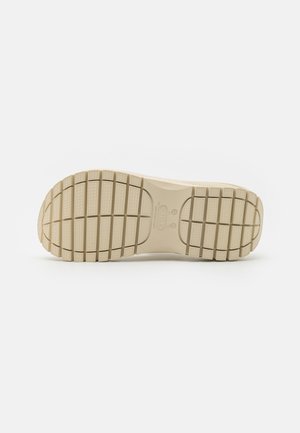Semelle de chaussure en caoutchouc beige avec des rainures texturées. Comprend un talon lisse et arrondi ainsi qu'une partie avant plate pour la stabilité et l'adhérence.