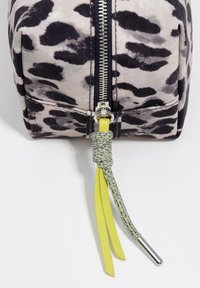 Czarny i beżowy woreczek w panterkę z metalicznym zamkiem błyskawicznym, ozdobiony zielonym akcentem węzłowym oraz żółtymi frędzlami na suwaku.