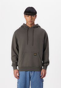 Dark olive green hoodie made of cotton blend, featuring a front kangaroo pocket, drawstrings, and a small yellow brand tag.