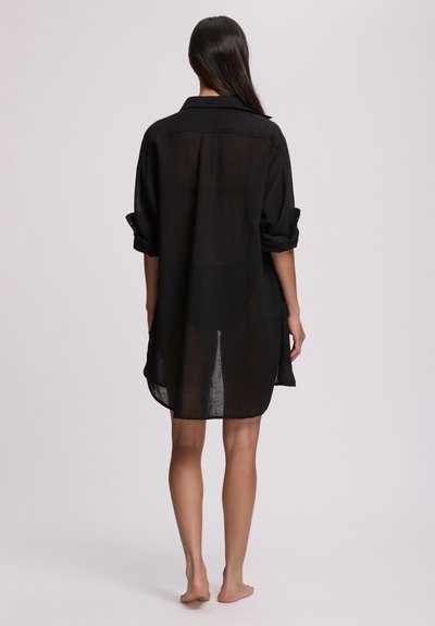 Μαύρο, διάφανο πουκάμισο με μακριά μανίκια, φαρδιά εφαρμογή, γιακά και μανσέτες που έχουν γυριστεί. Το τελείωμα φτάνει μέχρι το μέσο του μηρού, λίγο πιο μακρύ στο πίσω μέρος. Λείο ύφασμα.