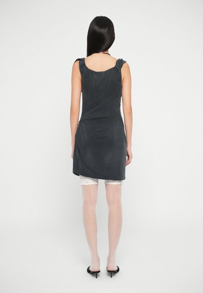 Vestido cinza sem mangas com detalhes de ombreira em babados, tecido fluido e corpete ajustado. Usado sobre calções brancos de renda.
