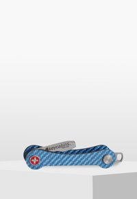 Multiverktyg nyckelring gjord av blå kolfiber med ett blad i rostfritt stål. Har en röd Schweizisk kors-logotyp och en elegant, böjd design.