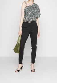 Blommig, enaxlad topp med volangdesign; svarta skräddarsydda byxor; grön mockaväska; svarta rehelsandaler med små gyllene detaljer.