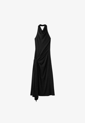Czarna sukienka maxi z odkrytymi ramionami, z drapowaną tkaniną zebrana i zawiązana na lewym biodrze, tworząca asymetryczną sylwetkę.