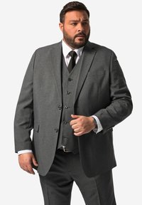 Grau Anzug bestehend aus drei Teilen mit Reverskragen, aus strukturiertem Stoff, mit Brusttasche und Knopfakzenten, kombiniert mit einem weißen Hemd und einer schwarzen Krawatte.
