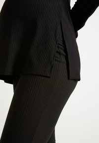 Svart ribbad tunika med sidosprund, tillsammans med matchande ribbade leggings. Tyget har en texturerad stretchfinish.