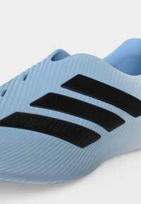 Ανοιχτό μπλε παπούτσι τύπου slip-on με υφή στην επιφάνεια και τρεις μαύρες διαγώνιες ρίγες στο πλάι.
