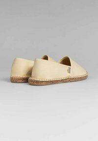 Espadrilles de lona beige con punta redonda y cerrada, y paneles laterales elásticos. La suela de cuerda presenta costuras alrededor del borde. Diseño clásico.