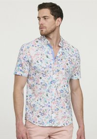Korte mouwen overhemd met knoopsluiting in lichte stof, met een bloemenpatroon in roze, blauw en groen op een witte achtergrond.