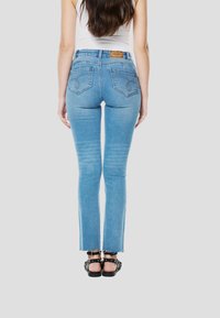 Lichtblauwe denim jeans met rechte pijpen, een rafelige zoom en achterzakken met decoratieve stiksels. Gemaakt voor dragen met zwarte sandaaltjes met bandjes.