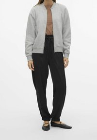 Szara kurtka bomberka na brązowym topie, do tego czarne spodnie dresowe z elastycznym paskiem w talii. Całość uzupełniają czarne płaskie buty.