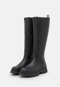 Bottes noires montantes en cuir lisse, avec une semelle épaisse et une boucle à l'arrière pour un enfilage facile.