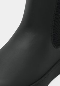 Sorte gummistøvler til anklerne med en glat overflade, rund form og mesh-sidedele for åndbarhed. Gummisål med syninger.