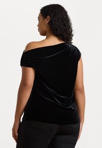 Svart sammetsblus med off-shoulder design och korta ärmar, med lös passform och sidofickor som framhäver den mjuka texturen och draperingen.