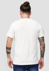 Hvid bomulds t-shirt med korte �ærmer, standard pasform og en glat tekstur. Udstyret med synlige tatoveringer på højre arm og ryg.