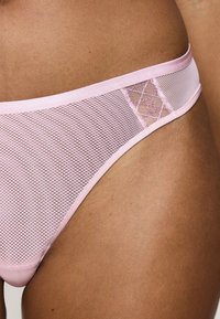 Jasnoróżowe stringi z siateczki z satynowym paskiem w talii, z wzorzystym detalem w siateczce dla dodatkowej tekstury. Gładki i oddychający materiał.