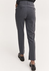 Grå skräddarsydda byxor med rak skärning, med två bakfickor och sidofickor vid fållarna. Materialet har en subtil textur.