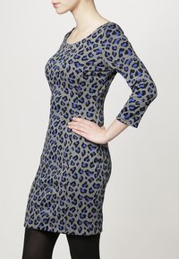 Robe grise avec un motif léopard en bleu et noir. Dotée d'un col rond et de manches trois-quarts. Design ajusté.