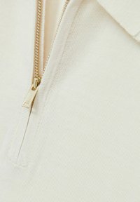 Sweatshirt crem cu fermoar, cu guler, fabricat dintr-un material cu textură fină de rib, având un fermoar din metal aurit. Prezintă un design cu guler înalt pentru o căldură suplimentară.