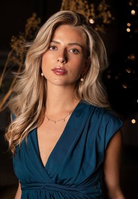Teal dress with a deep V-neck and braided waist detail, paired with gold and pearl drop earrings, set against a dark background with soft lights.