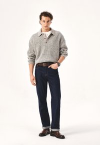 Grauer Strickpullover mit Kragen, Knopfdetails, kombiniert mit dunkelblauen Jeans und braunen Leder-Stiefeletten. Schlichtes weißes Unterhemd.