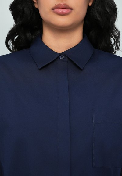 Camicia blu con bottoni, realizzata in tessuto liscio, con colletto a punta, una tasca sul petto e un taglio dritto.
