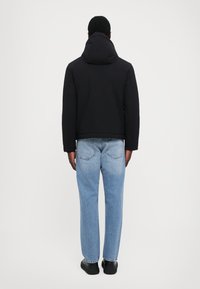 Jachetă neagră, căptușită, cu glugă, asociată cu blugi deschiși la culoare, cu tăietură lejeră. Design simplu, cu detalii minime, purtată cu încălțăminte neagră.