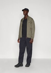 Πράσινο-ελαιί ένδυμα με φερμουάρ, μαύρο T-shirt, ναυτικό μπλε παντελόνι και μαύρα παπούτσια. Διαθέτει υφή υφάσματος και μπροστινές τσέπες. Καθημερινή ένδυση για εξωτερικούς χώρους.